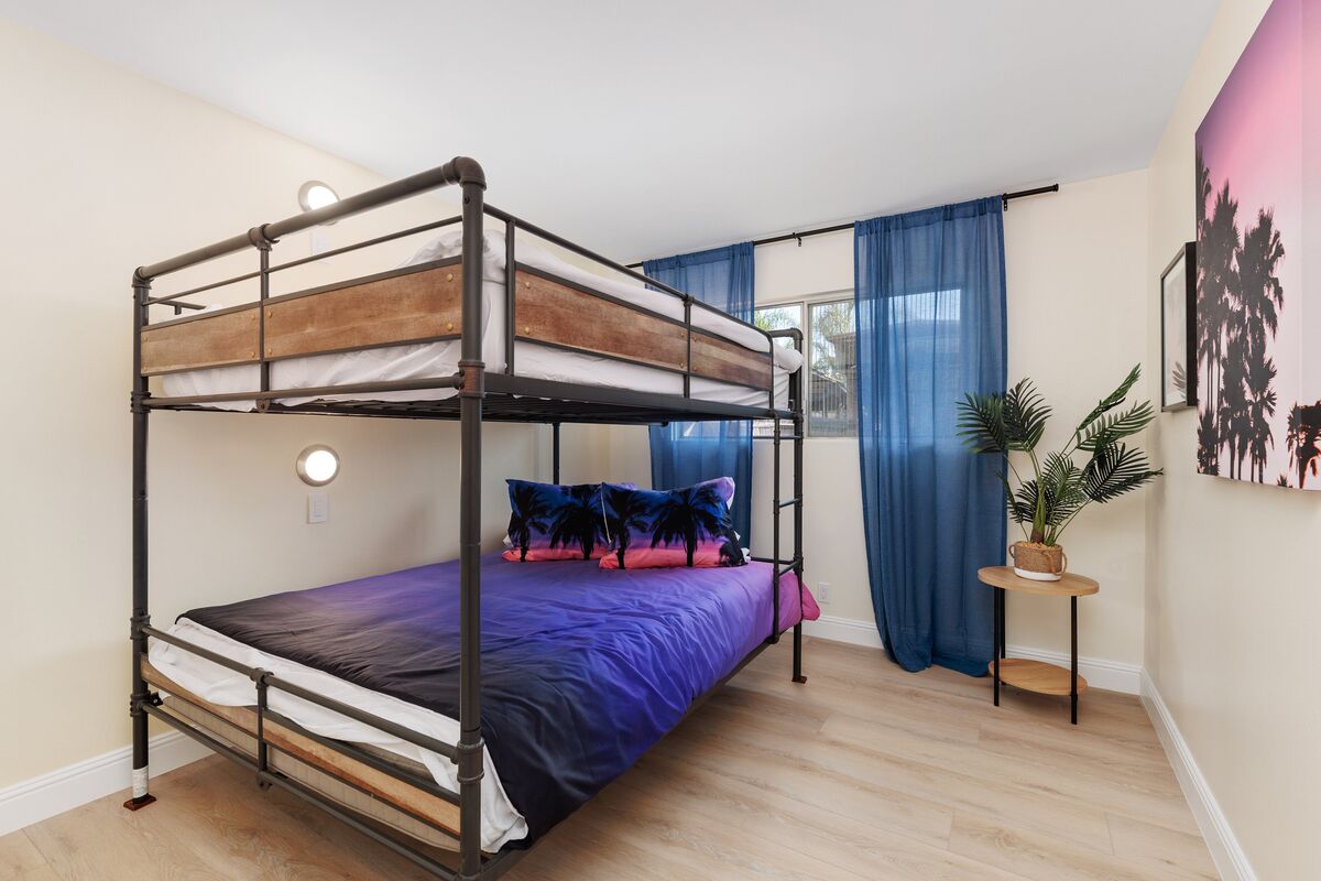A bunk bed room with a wooden frame, a purple bedspread, and a small table with a plant.