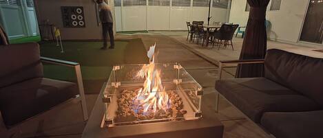 An outdoor patio area with a glass-top fire pit, outdoor furniture, and string lights.