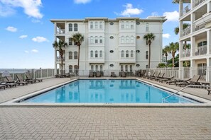 A swimming pool with lounge chairs and a building with balconies.