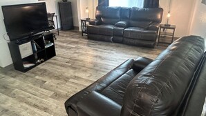 A living room with a black leather sofa, a flat-screen TV on a stand, and a wooden floor. - Beach/Kenai Center 5 minutes (Kenai)