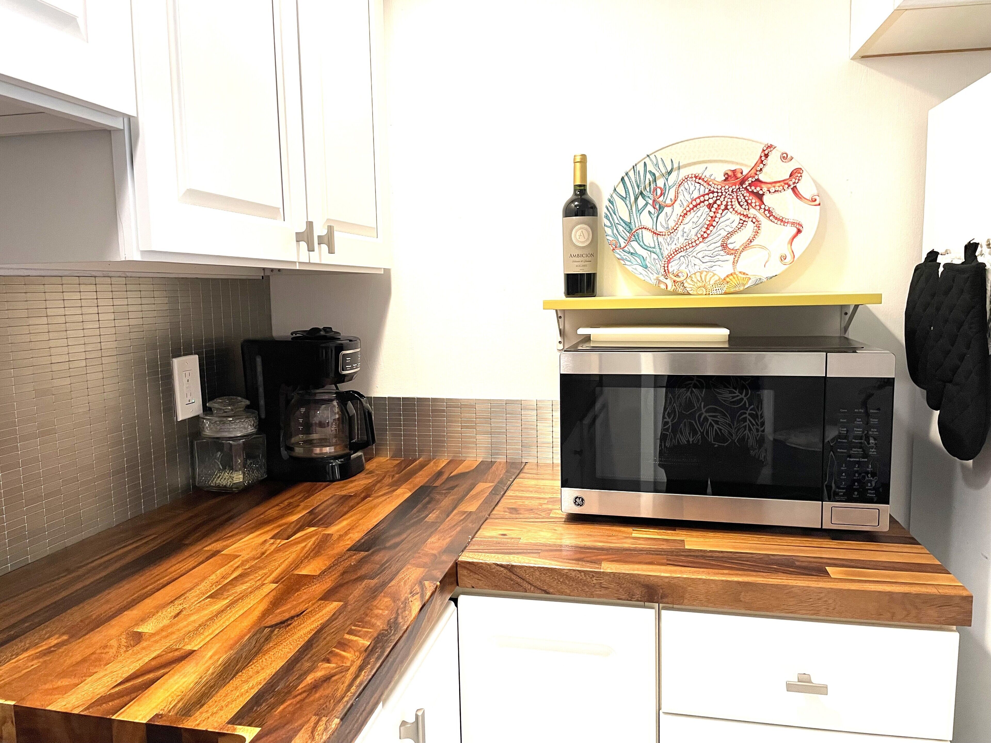 Eine Küche mit einer Holzausziehtafel, einer Kaffeemaschine, einer Mikrowelle und einer Weinflasche.