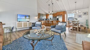 A spacious living room with a glass coffee table, a television, and a dining area with a wooden table and chairs.