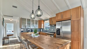 A spacious kitchen with a large island, wooden cabinets, stainless steel appliances, and pendant lighting.