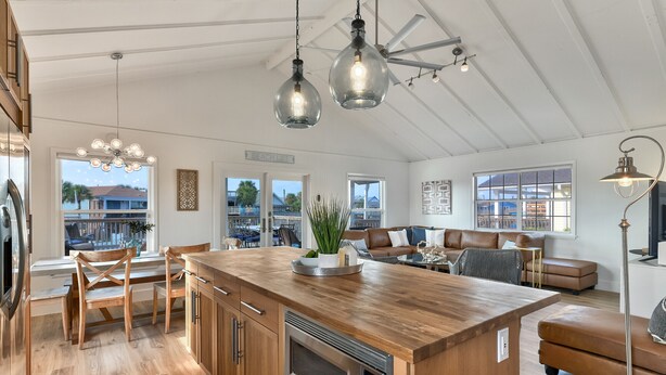 A spacious kitchen with a wooden island, modern pendant lights, and a view of the beach.