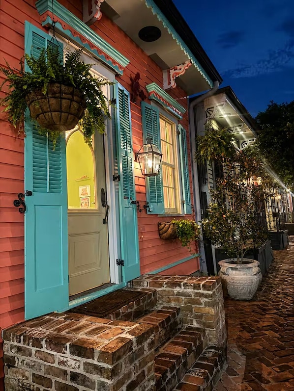 A building with a brick entrance, teal shutters, and hanging planters.