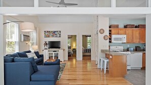 Ein modernes Wohnzimmer mit einem blauen Sofa, einem Fernseher und einer Küchenzeile mit Holzschränken und einer Mikrowelle.