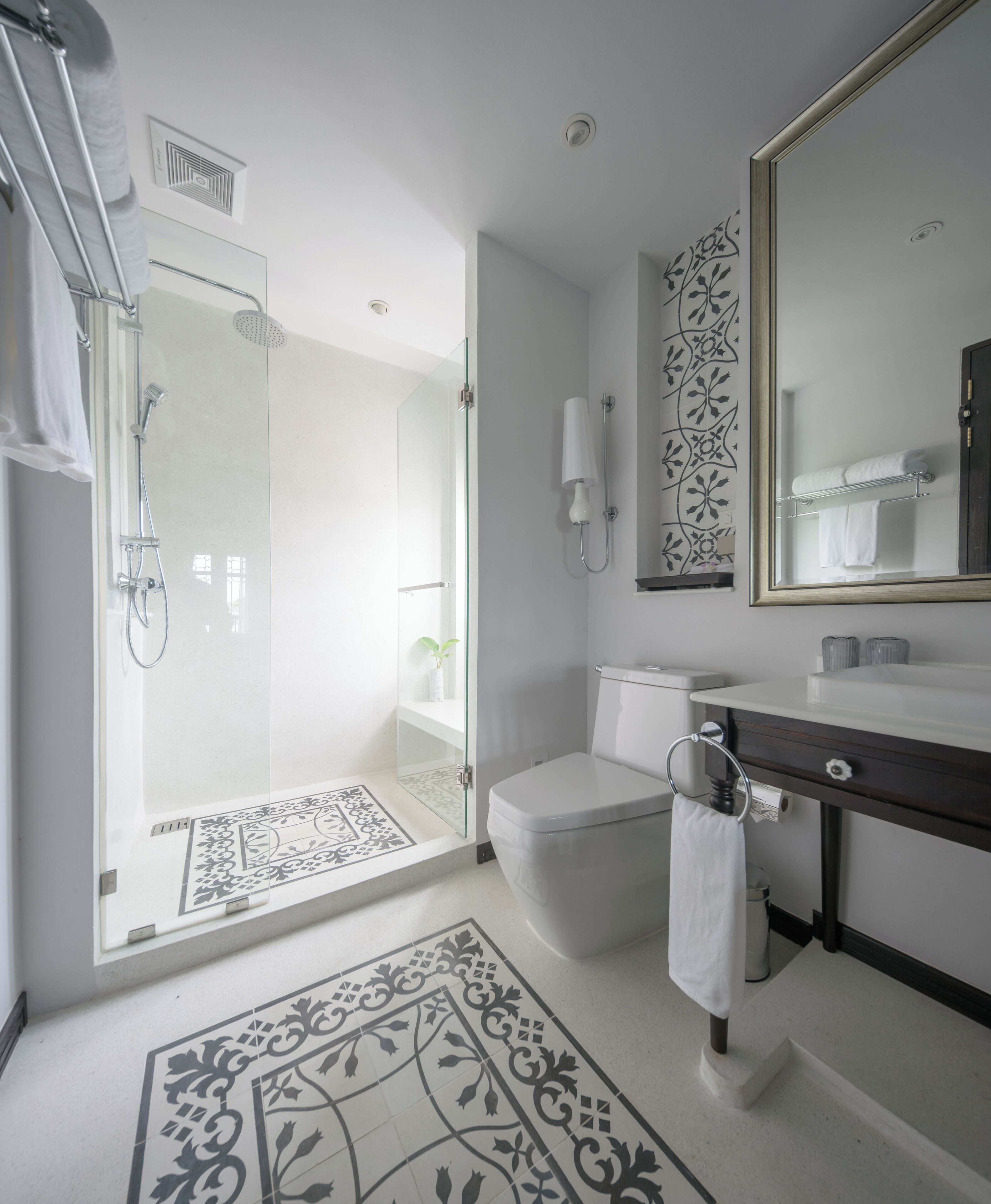 A modern bathroom with a glass-enclosed shower, a toilet, a sink with a dark countertop, and a large mirror.