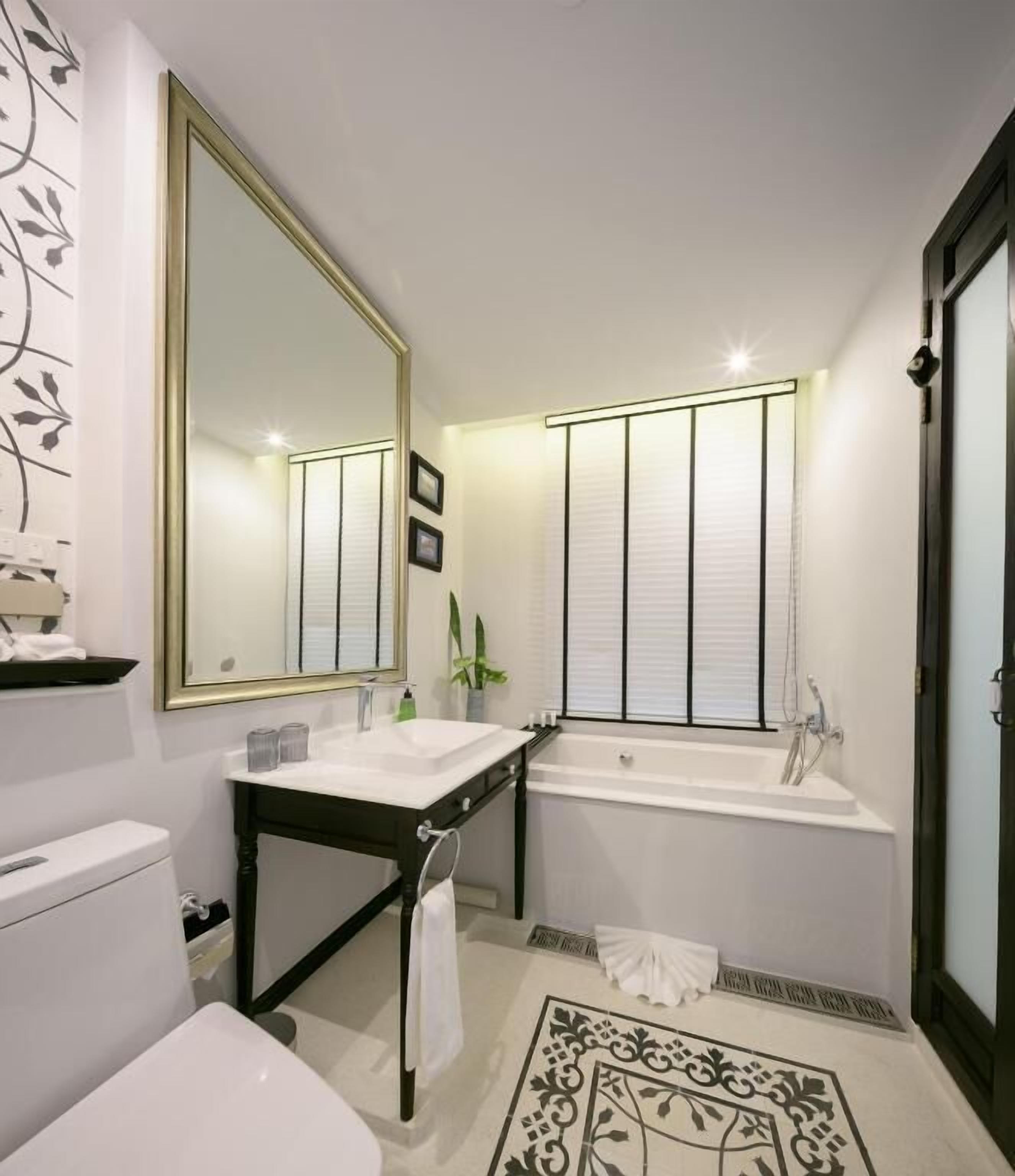 Un baño moderno con un lavamanos blanco, un espejo grande, una bañera y un tapete decorativo.
