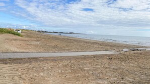 A sandy beach with a paved walkway leading to the water, a few people in the distance, and a line of buildings along the shore. - Awesome home in Falkenberg with WiFi (Falkenberg)