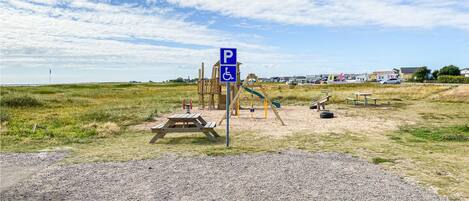 A parking sign with a wheelchair symbol, a picnic table, playground equipment, and a gravel path.