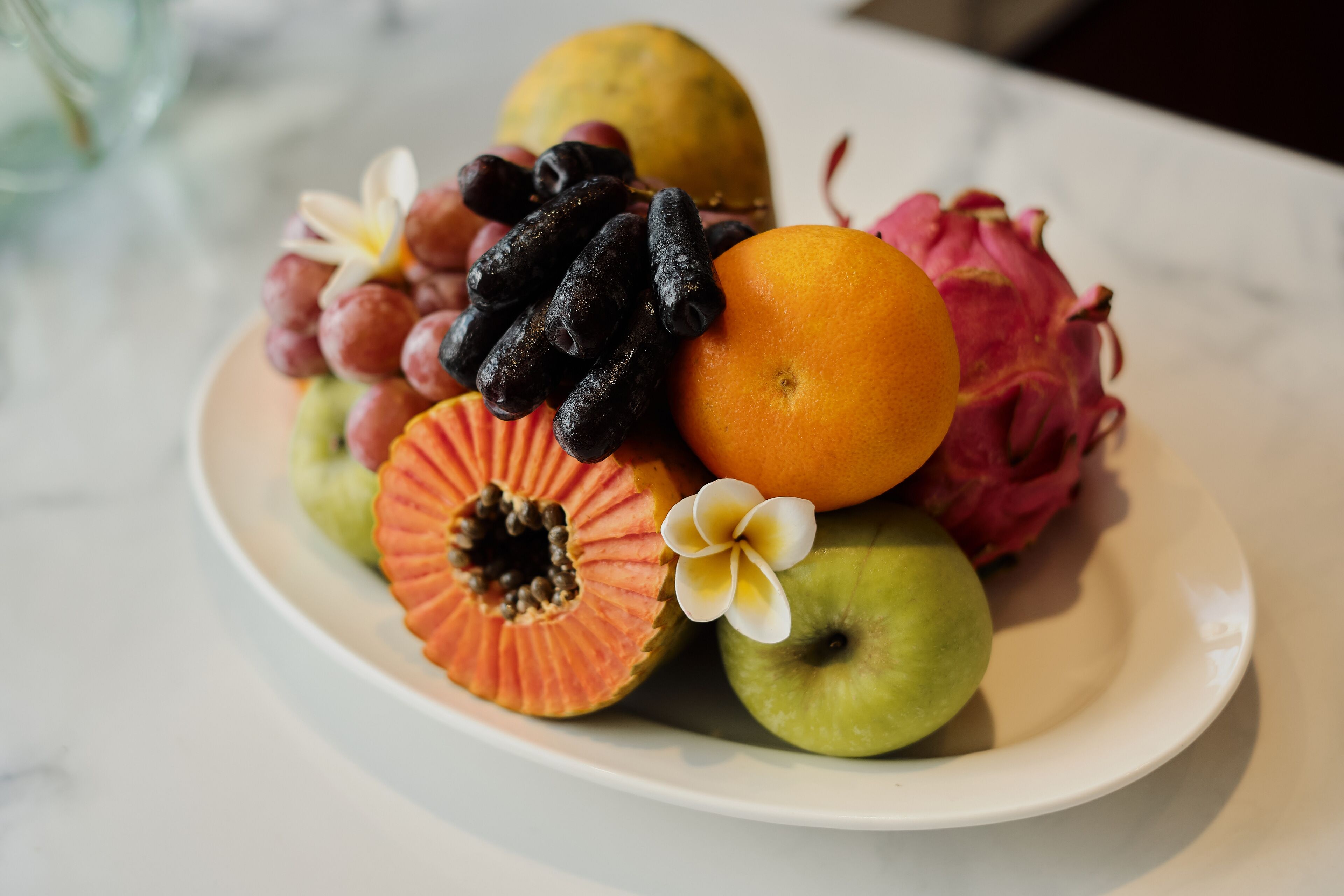 A plate of assorted fruits including a dragon fruit, mango, apple, and grapes.