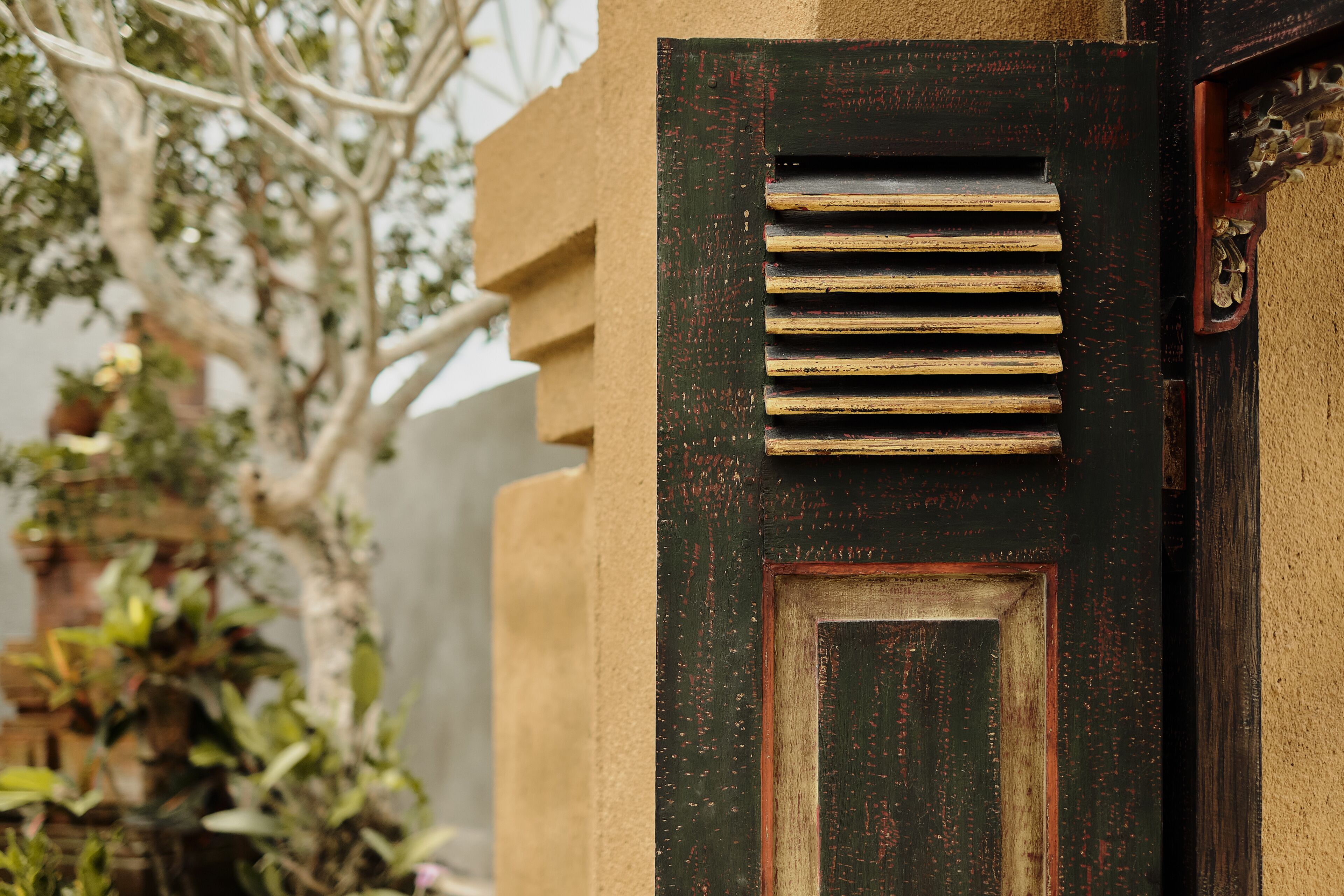 A door with horizontal slats and a small window, set in a textured wall.