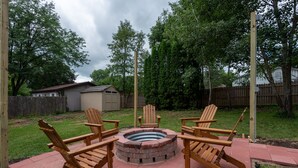 Een achtertuin met een vuurkorf en houten stoelen.