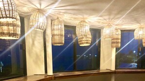 A bar area with patterned floor tiles, wooden stools, and hanging wicker lamps. - Rum Punch Lodge (Corozal)