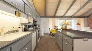 A compact kitchen with grey cabinets, a microwave, and a sink. There's a dining area with a yellow table and chairs, and a window with curtains. - Secluded wine country retreat,  full kitchen (Arroyo Grande)