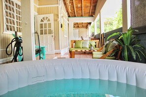 Un área de piscina con terraza de madera, un sofá verde y una planta en maceta.