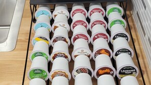 Eine Kaffeemaschine von Keurig und ein Vorratshalter für Kaffeekapseln mit verschiedenen Markenprodukten.