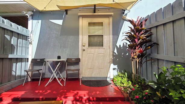Eine kleine Terrasse mit rotem Boden, einem Tisch, zwei Stühlen, einer Tür und einem Holzzaun.