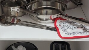 Eine Küche mit Edelstahl-Töpfen, Pfannen, einem Toaster und einem Slow Cooker auf einem weißen Regal.