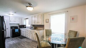 Una cocina moderna con armarios blancos, un refrigerador negro, una mesa de vidrio con cuatro sillas y una ventana con cortinas.