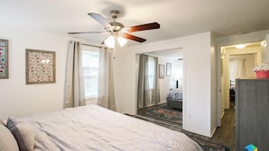 Un dormitorio con cama, ventilador de techo y vista a otra habitación.
