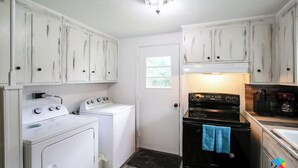 Cocina compacta con muebles blancos, lavadora, estufa y cafetera.