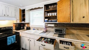 Una cocina con armarios blancos, estufa negra, microondas y lavamanos.