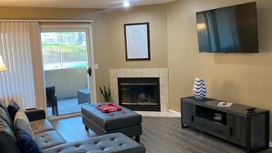 A living room with a sofa, ottoman, fireplace, TV, and a sliding glass door leading to an outdoor area. - Weekend Wine Getaway (Temecula)