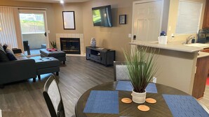A modern living room with a fireplace, a dining area with a round table, and a kitchen area with a countertop and sink.