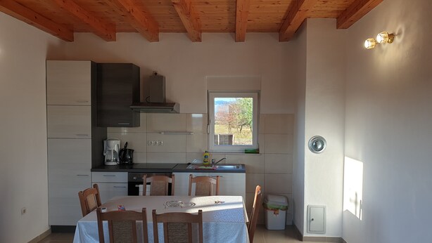A compact kitchen with modern appliances, a dining table with chairs, and a window with a view of trees. - Impeccable 2-Bed House in Privlaka, Croatia (Privlaka)