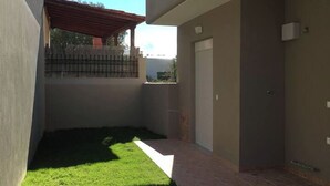 A small, enclosed outdoor area with a paved floor, a grassy patch, and a red-roofed structure.