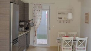 A kitchen with a refrigerator, a sink, and a dining area with white chairs and a table.