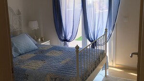 A bedroom with a bed, a nightstand, a lamp, and sheer curtains.