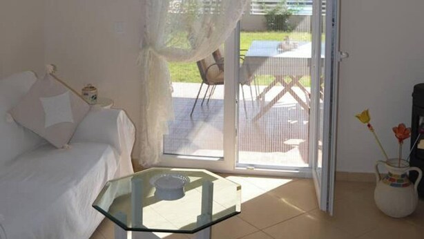 A room with a glass-top table, a white sofa, and a sliding glass door leading to an outdoor area with a table and chairs.