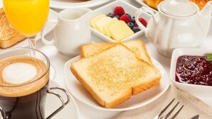Un desayuno con tostadas, mantequilla, mermelada, café y jugo.
