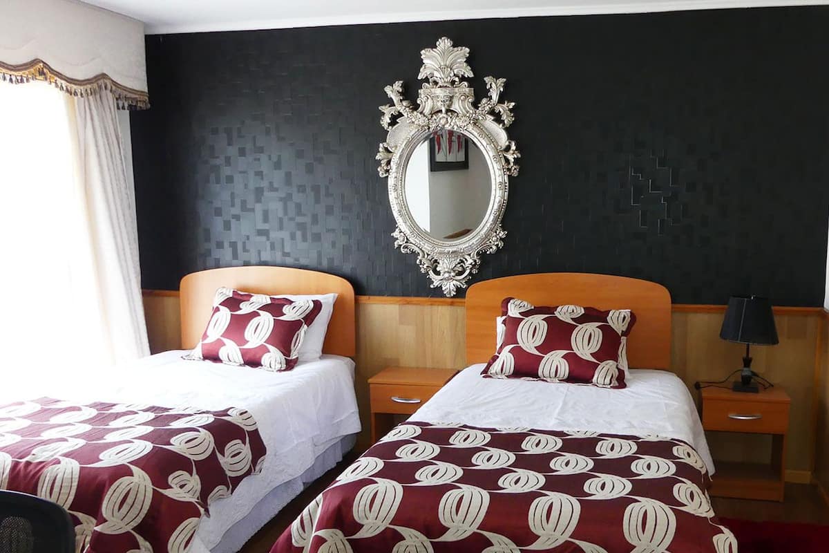 Ein Hotelzimmer mit zwei Betten, jeweils mit einem gemusterten Überwurf, einem großen, verzierten Spiegel und einem Nachttisch mit Lampe.