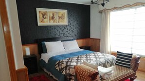 Un dormitorio con cama, mesita de noche, banco y ventana con cortinas.