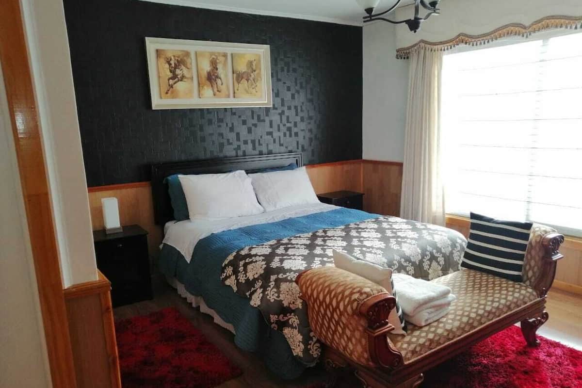 Ein Schlafzimmer mit einem Bett, einem Nachttisch, einer Bank und einem Fenster mit Vorhängen.