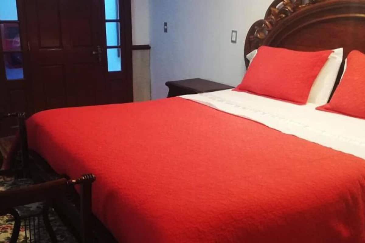 Ein Bett mit roter Decke, einem Holzkopfende und einem Nachttisch mit Lampe.