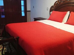 A bed with a red blanket, a wooden headboard, and a nightstand with a lamp. - Hotel Ruta Costera (Nueva Imperial)
