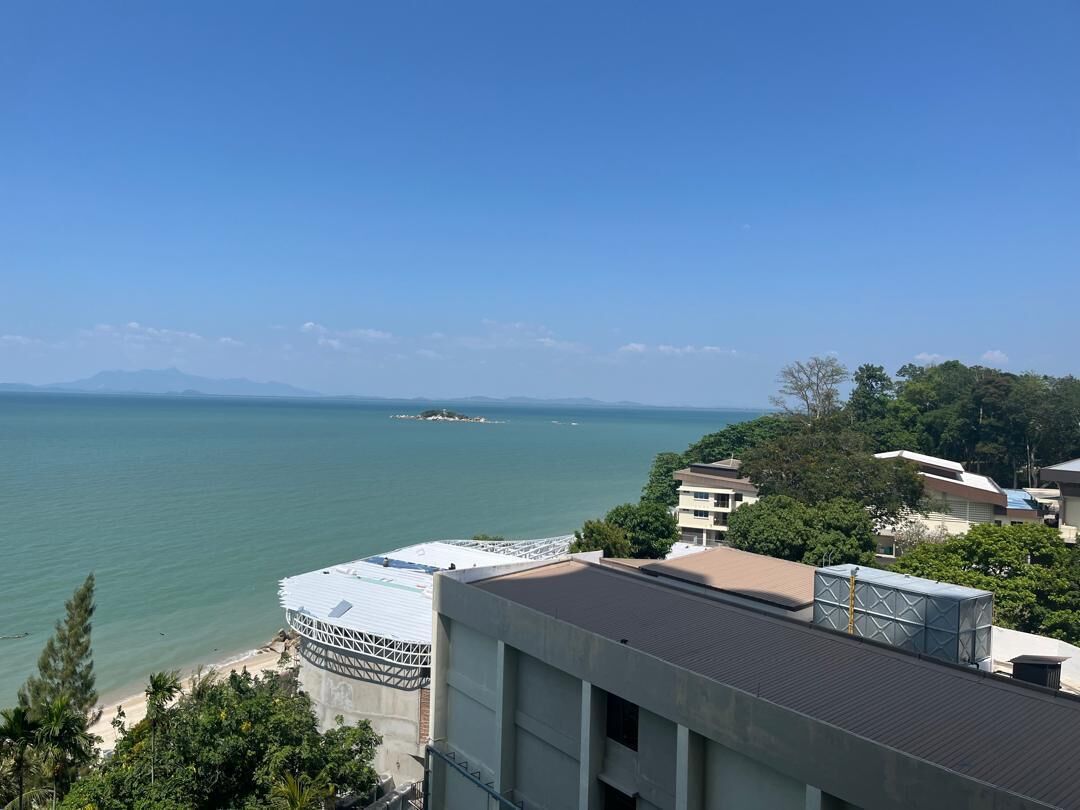 Une vue sur la côte, avec un bâtiment doté d’une terrasse sur le toit, un ciel dégagé et une ligne de côte lointaine.