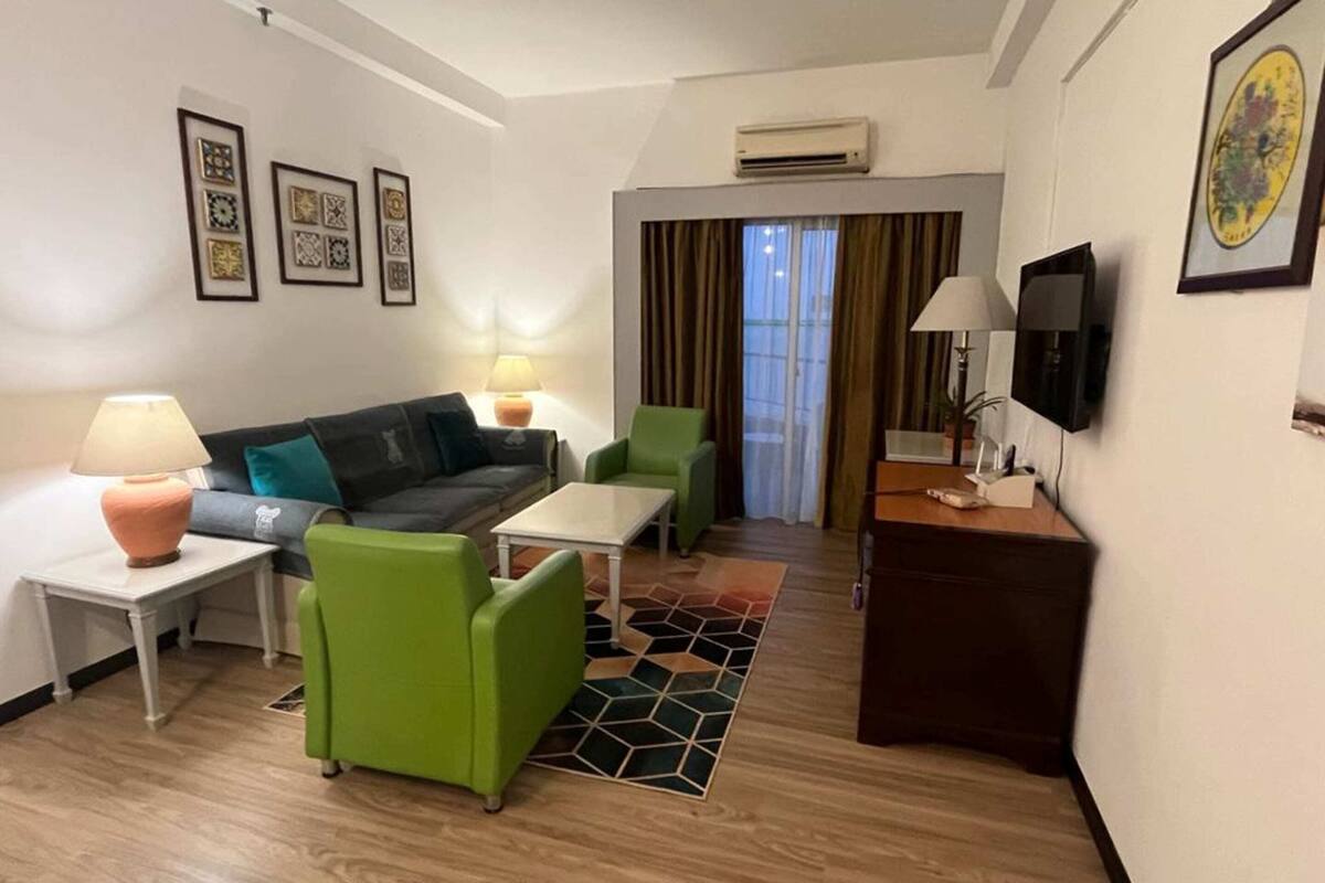 A modern hotel room with a sofa, chairs, a small table, a TV, and artwork on the walls.