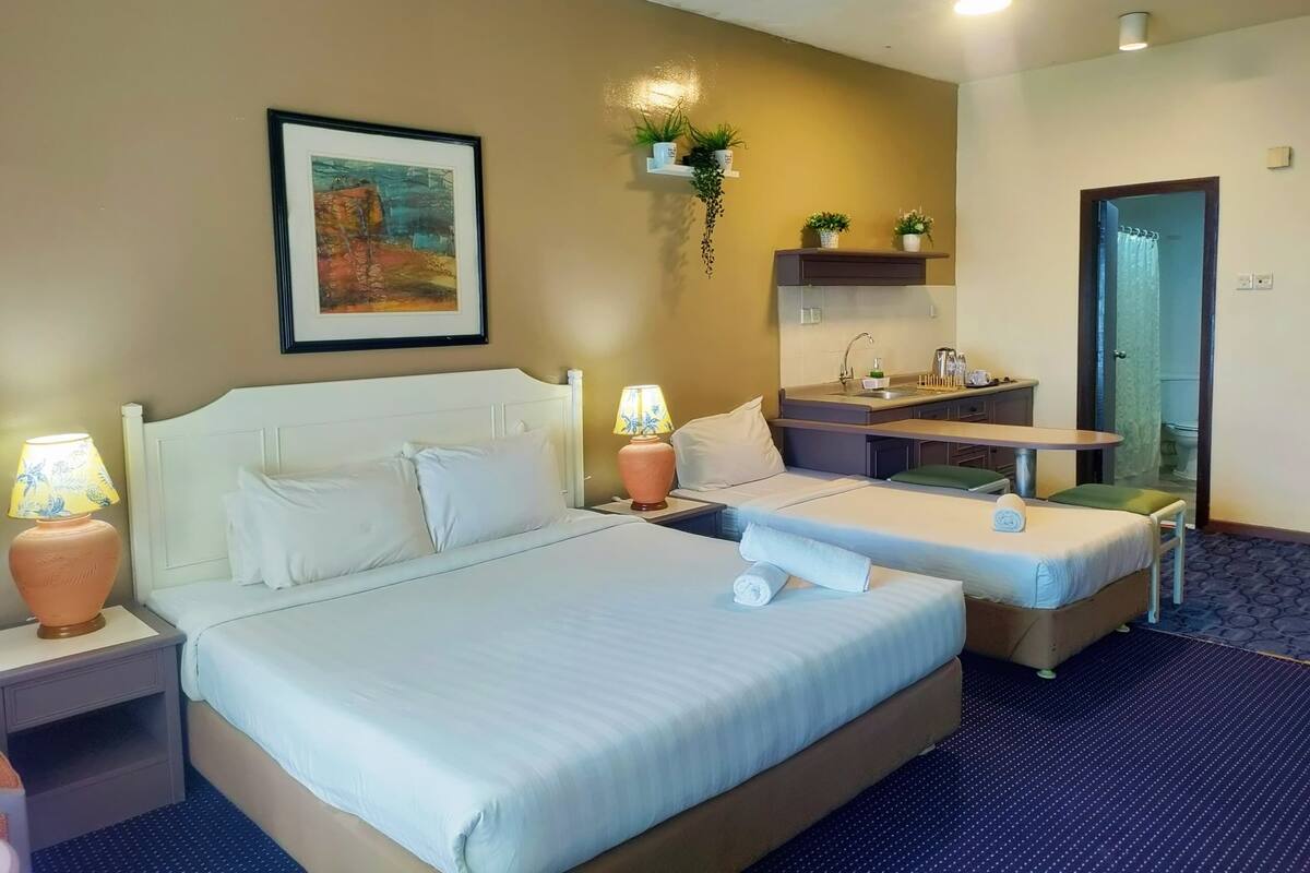 A hotel room with a large bed, a small desk, a sink, and a shower area.