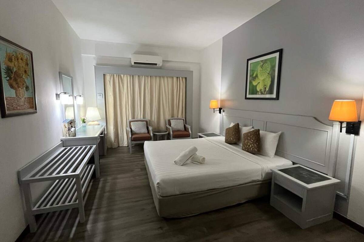 A hotel room with a large bed, two bedside tables, a desk with a chair, a small table with a lamp, and a chair.