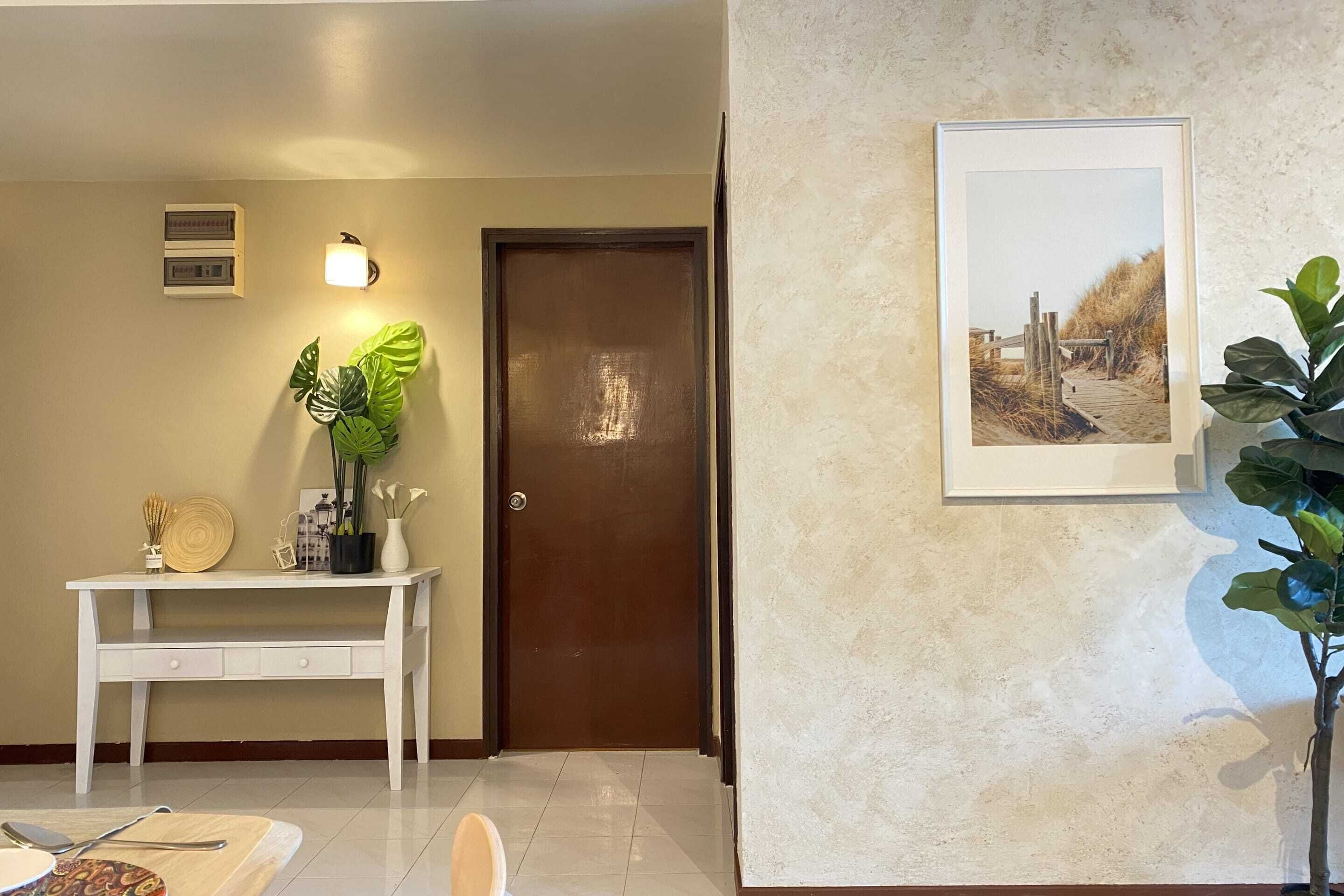 A hallway with a white desk, a potted plant, a framed picture, and a door.
