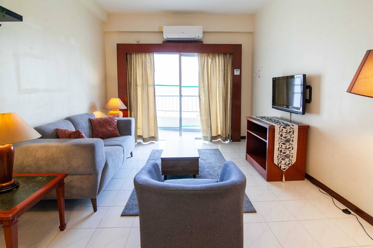 A living room with a sofa, armchair, TV, and a small table.