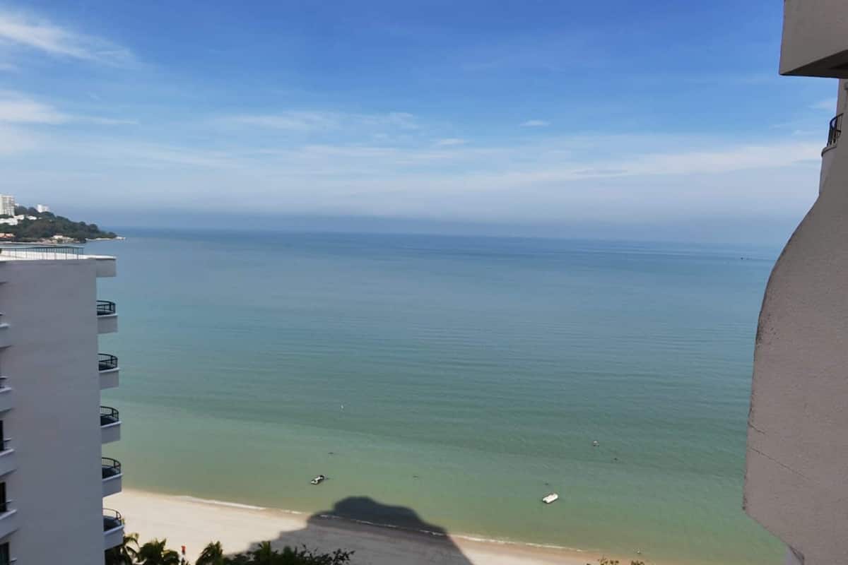 A coastal view from a balcony overlooking a beach with clear water and a distant shoreline.