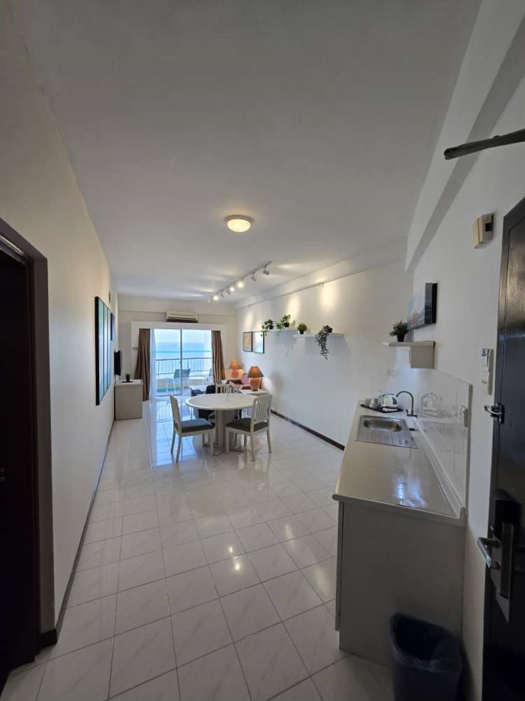A modern kitchen with a dining area, white tiled floors, and a view to the outside.