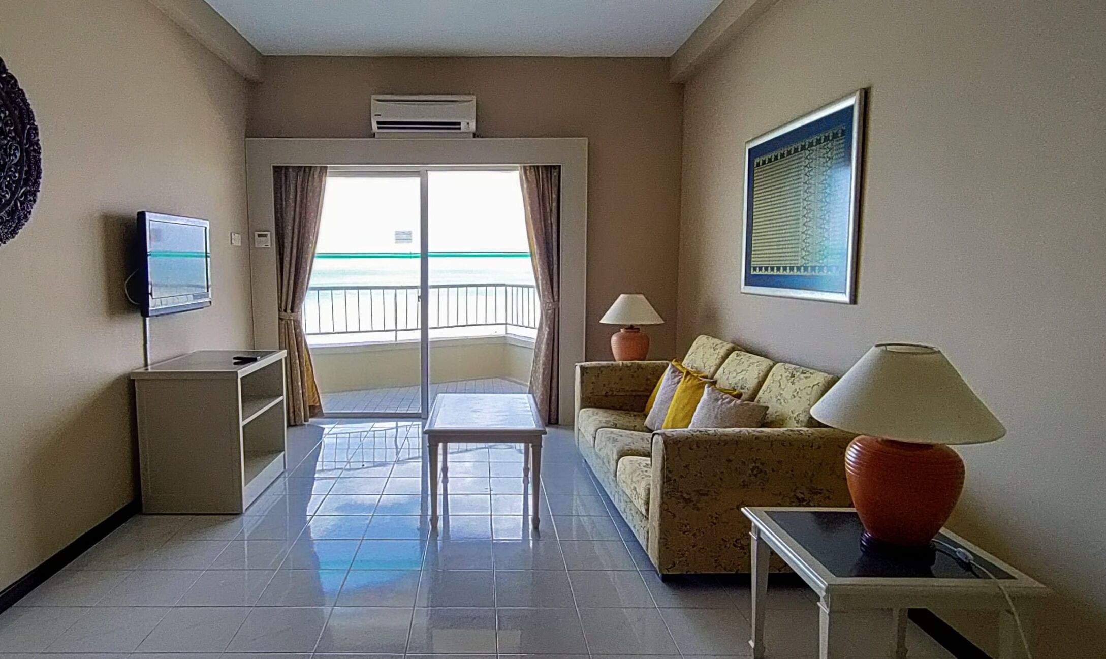Habitación de hotel con balcón, sofá, televisor, lámpara y un cuadro en la pared.