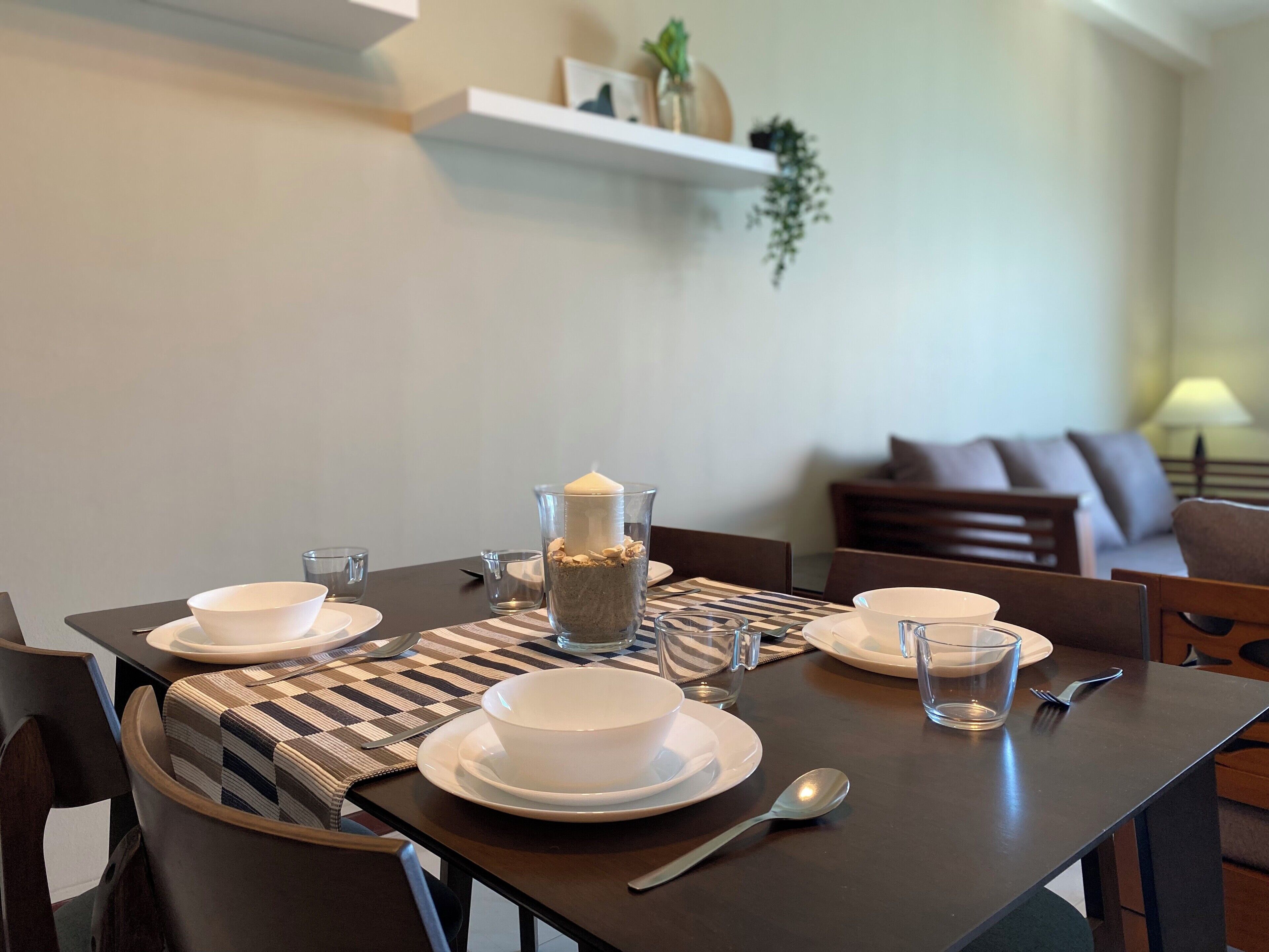 Een eettafel gedekt met witte borden, kommen en een kaars als middelpunt.